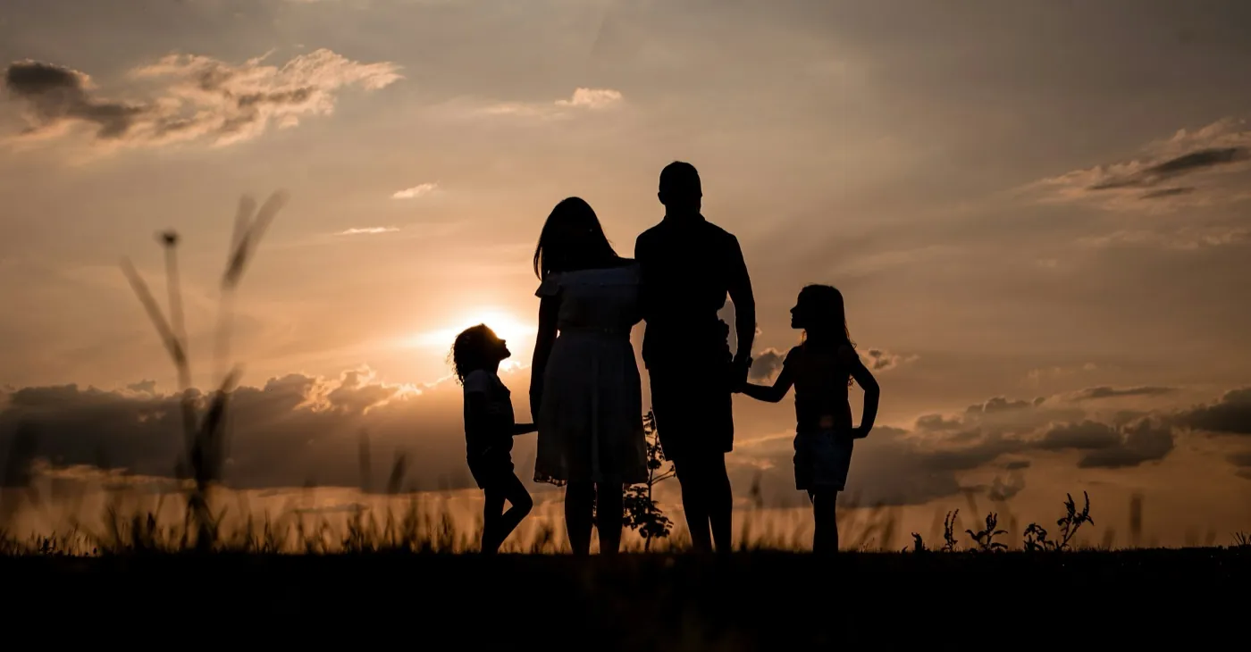 A family of four holding hands, silhouetted against a sunset