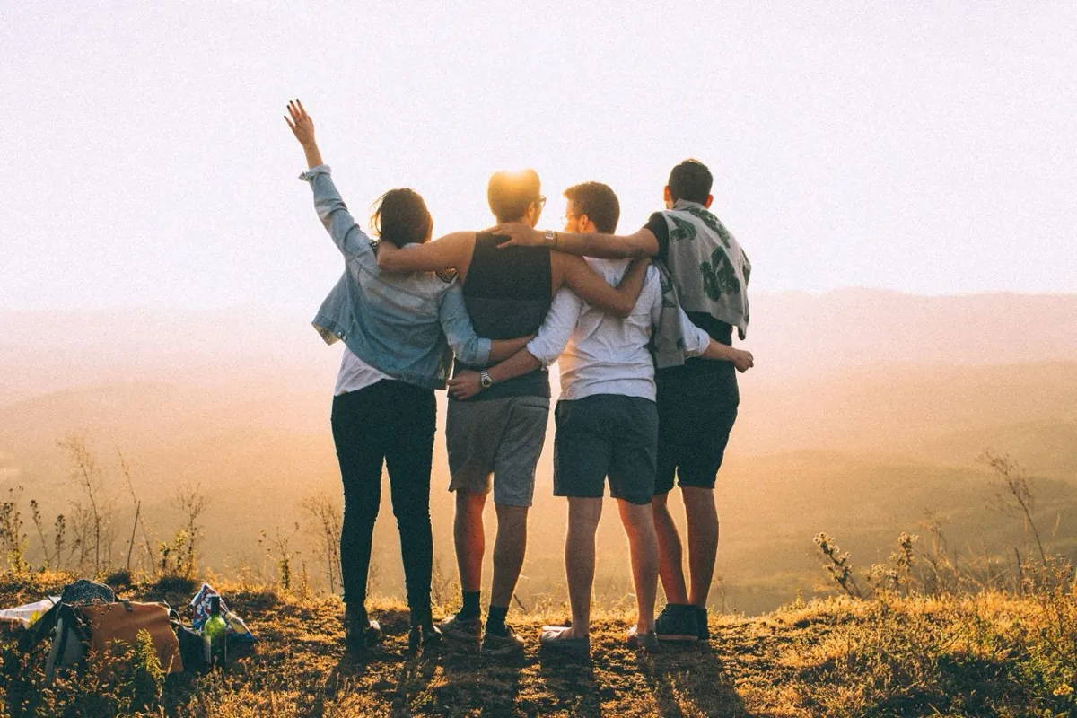 Four friends with their arms around each other, watching a mountain sunset